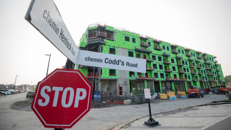 A building under construction on a city street corner, covered in green construction wrap.