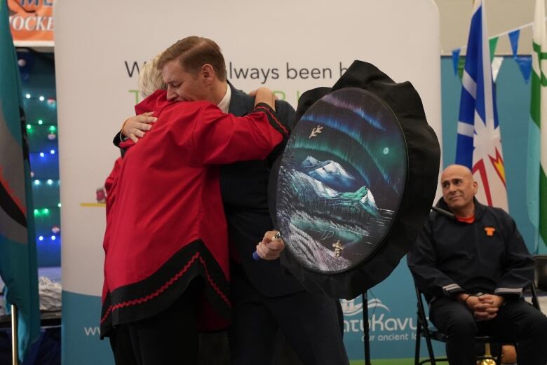 A man wearing a suit hugs a woman while holding a drum.