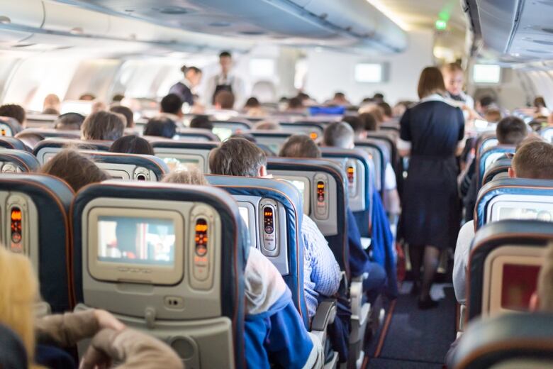 Interior of large passenger aircraft with passengers and flight attendants.