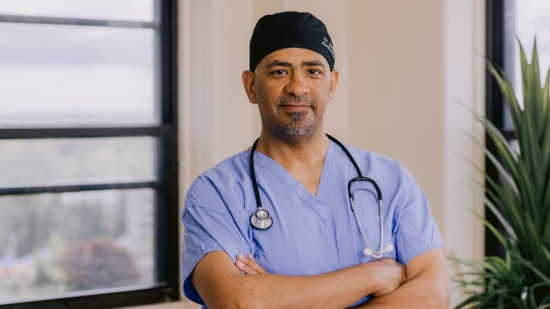 Man wearing scrubs and a stethoscope stands with his arms crossed.