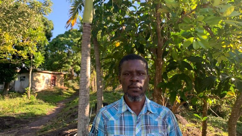 A man wearing a plaid shirt standing in front of trees.