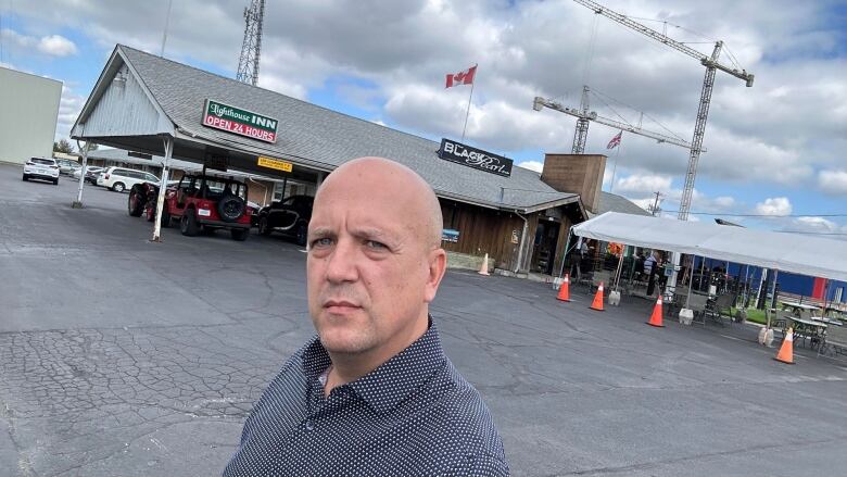 A bald man stands in front of the lighthouse inn and black pearl pub. 