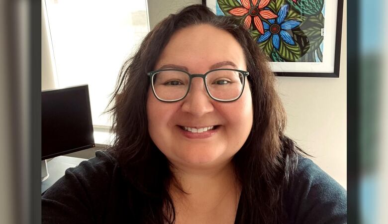 A woman with mid-length, brown hair and black-rimmed glasses is pictured smiling to the camera.