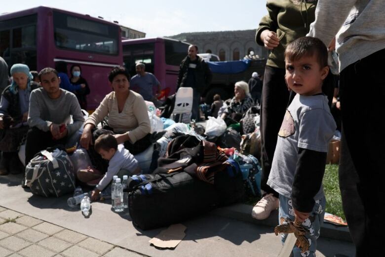 Refugees sit outside with their belongings.