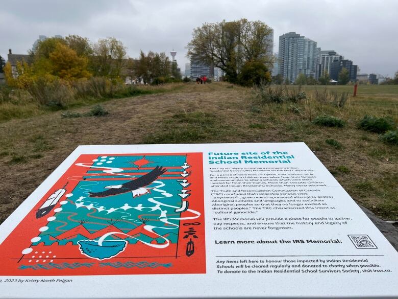 A marker with details on the future site of the Indian Residential School Memorial at Fort Calgary is seen on the ground with skyscrapers in the background.