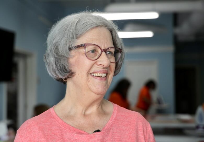 A woman wearing a pink shirt and glasses smiles to her right.