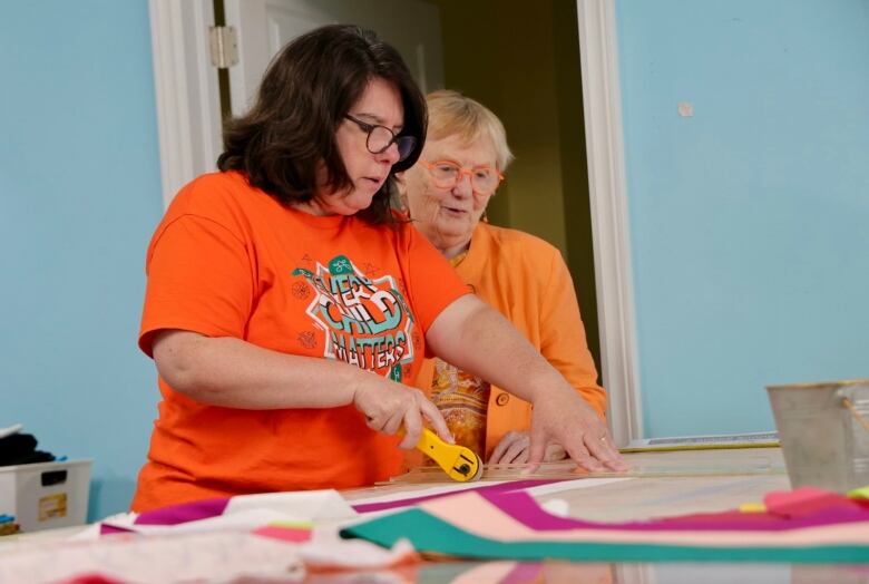 Two people wearing orange stand in front of a quilting table, looking down at some fabric. 