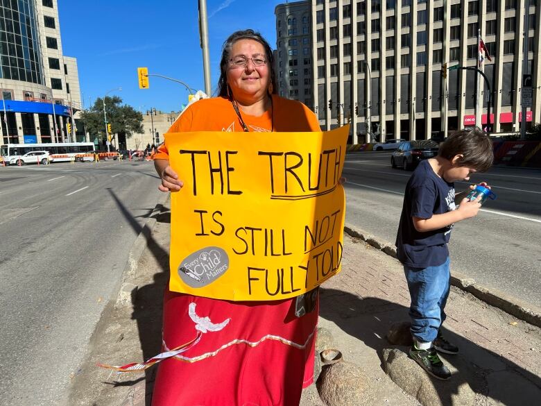 A woman wearing an orange shirt and holding a sign that says 