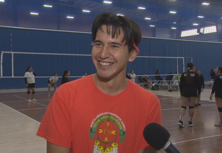 Tyler smiles during an interview while others play on the court behind him.