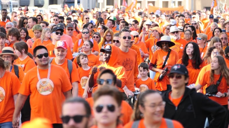 People wearing orange shirts walk in a crowd.