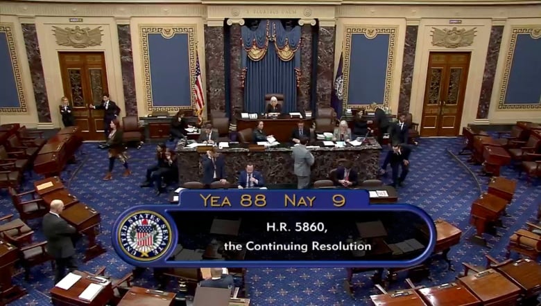 A still image from video shows the floor of the U.S. Senate with a graphic showing vote totals.