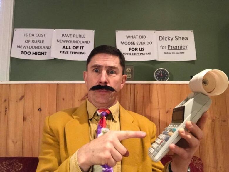 Blackmore is pictured here wearing a garish suit and brandishing an old fashioned calculator. Behind him are a number of signs, riddled with typos about rural Newfoundland. 