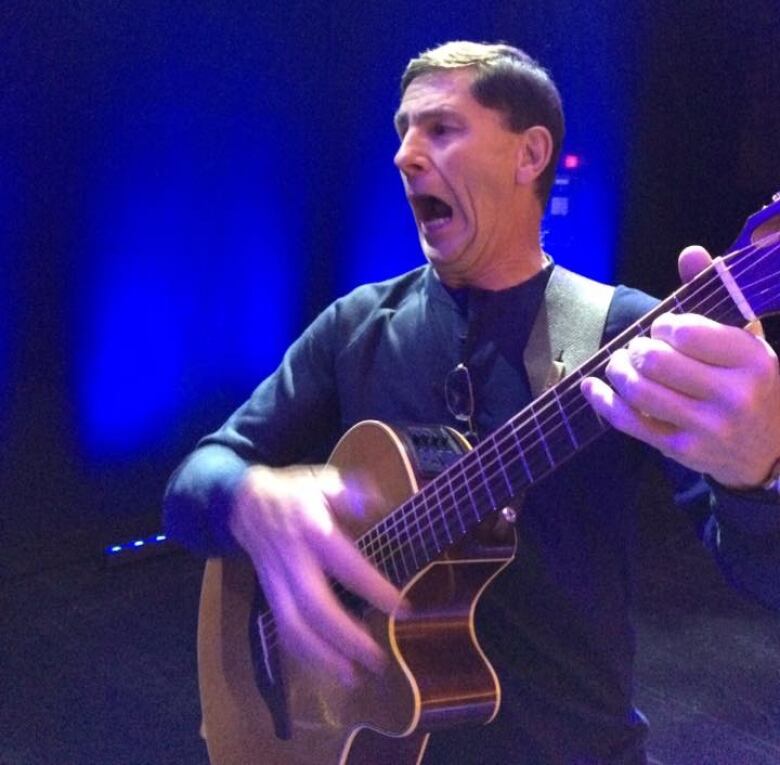 A man plays guitar while making a funny face. 