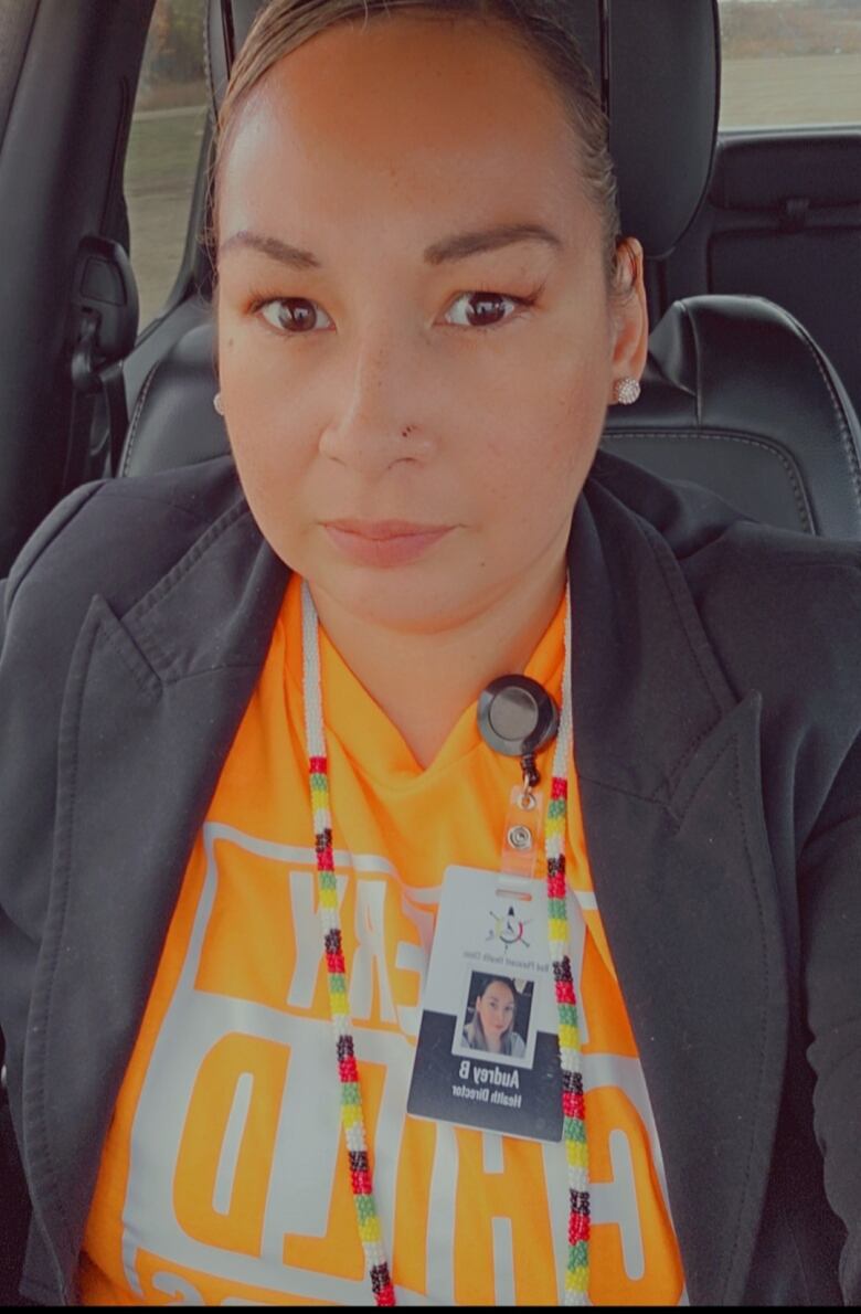 A woman in an orange shirt and black coat.