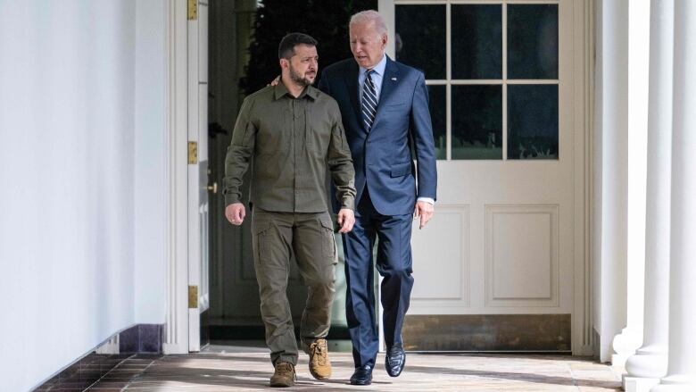 A person puts an arm around another person's shoulders as they walk down a hall.