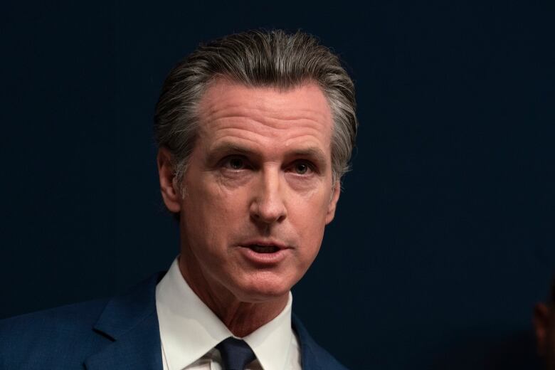 A man in a dark suit and tie answers questions from reporters.