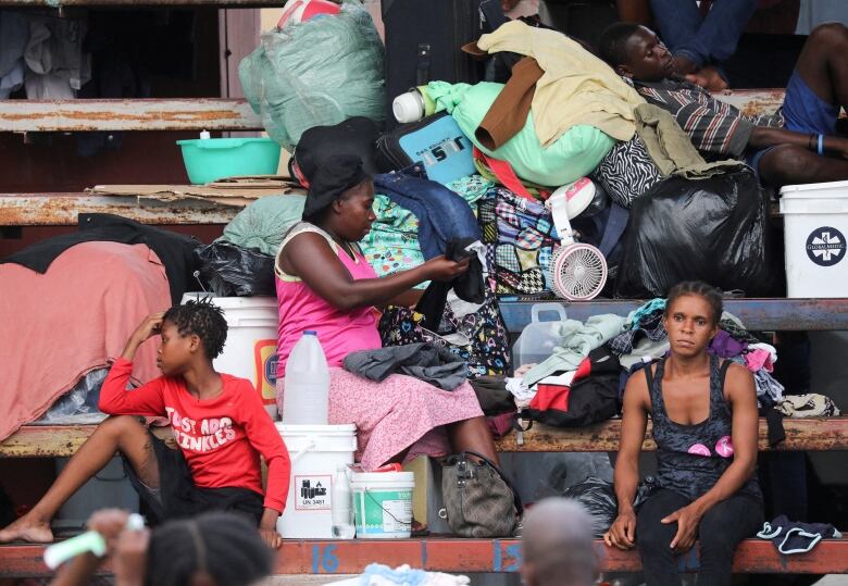 People surrounded by their possessions sit on wooden stairs