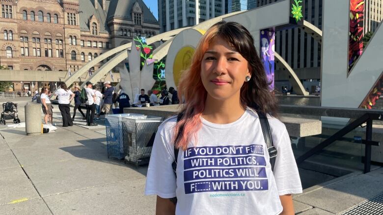 A woman stands near city hall in Toronto and poses for the camera in a white T-shirt.