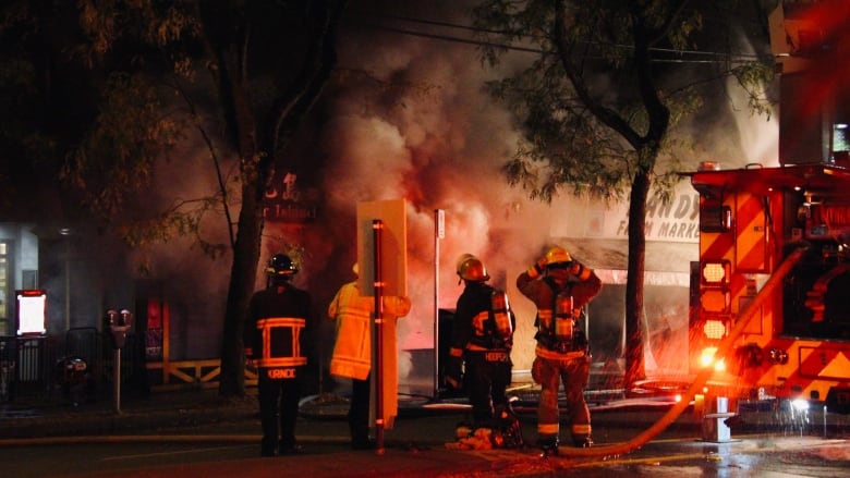 Smoke and flames engulf a business while firefighters stand on the street.