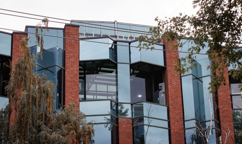 The upper part of a glass and brick building is shown against a cloudy sky.