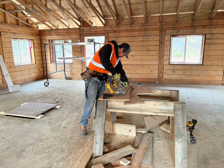 A man in a hi-vis vest cutting pieces of wood, inside a building site. 