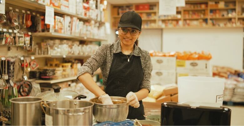 A worker at a Desi store in Regina makes some food in a metal bowl.