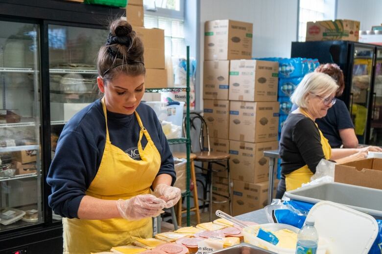 People wearing yellow aprons make sandwiches.