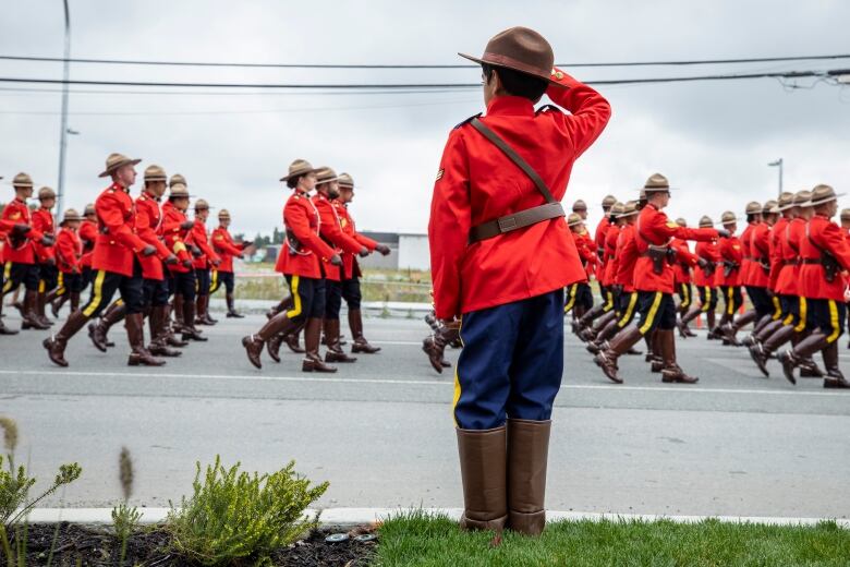 A boy wearing a Red Serge costume salutes a funeral procession of RCMP officers.