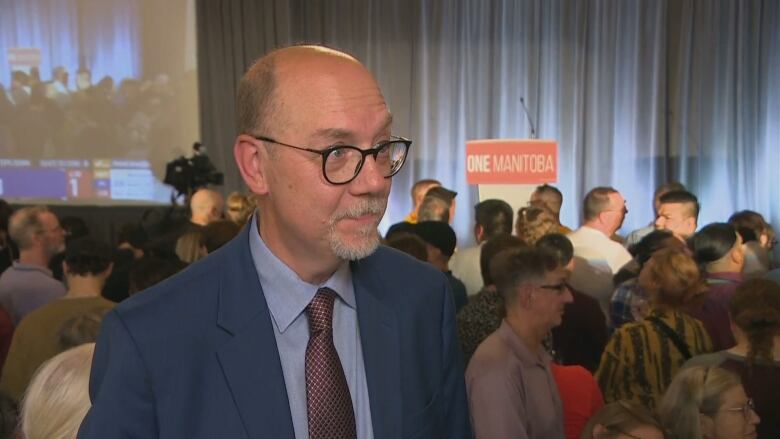 A man wearing glasses speaks to a reporter off camera. 