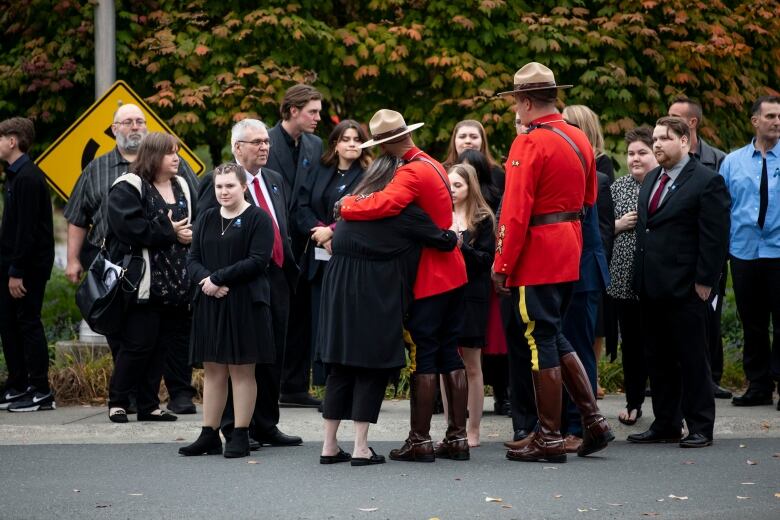 Two people in RCMP red hug mourners at a funeral.