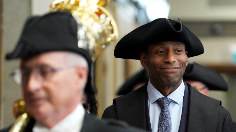 A legislature's speaker wearing a three-pointed black hat walks in a hallway.