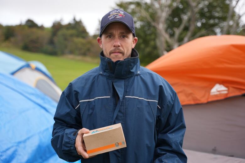 A man holding a box of fast food. He's standing in front of tents.