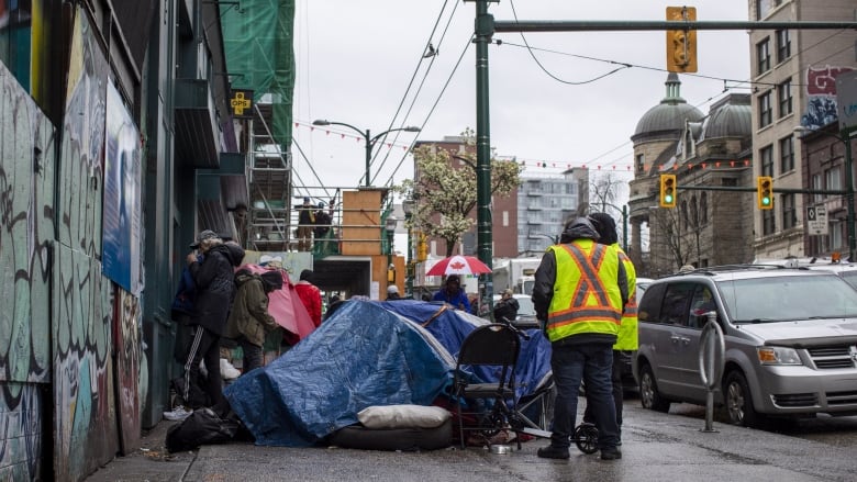 Men wearing safety vests take down a tent on a sidewalk.