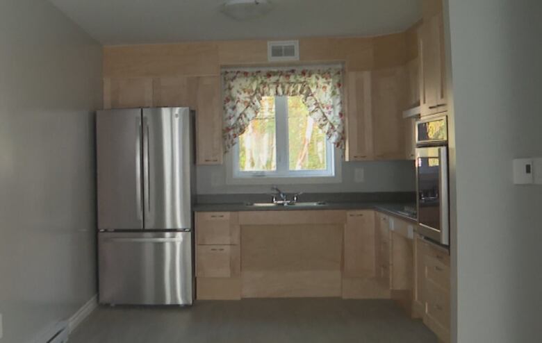 A kitchen with fridge, window, cupboards and oven.