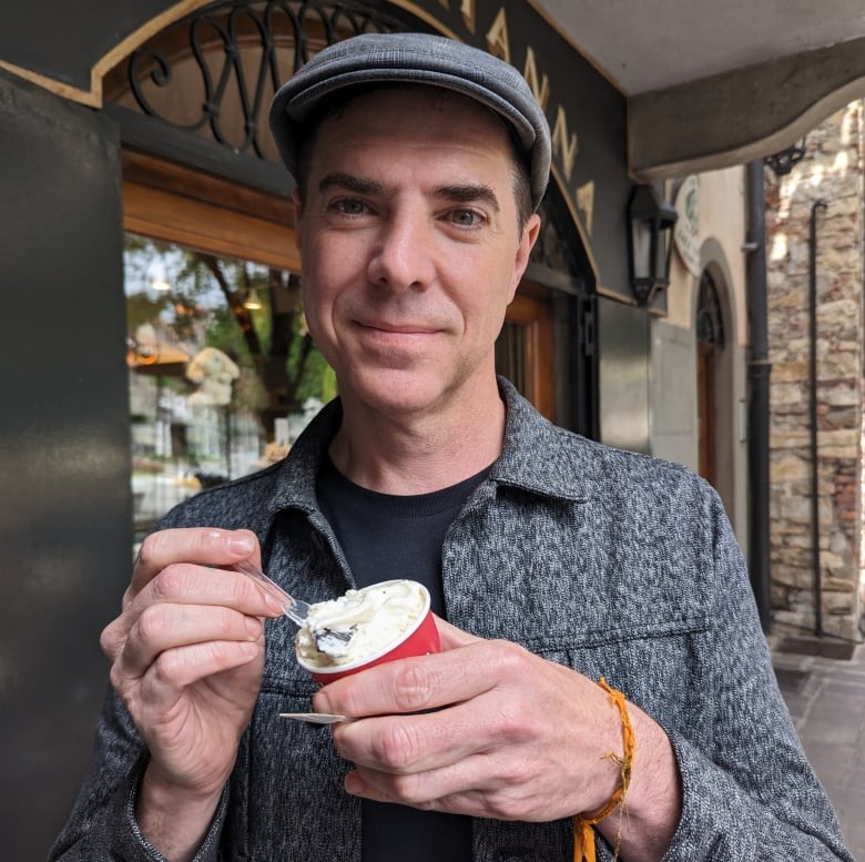 A smiling man poses holding a cup of ice cream in his hand.