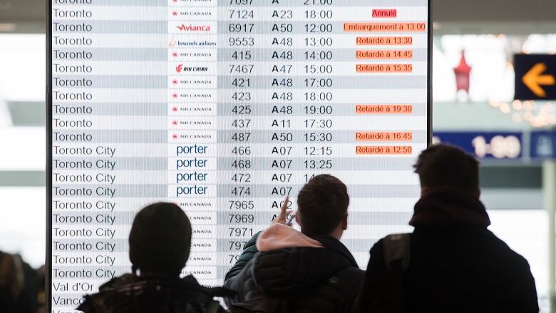 Passengers look at an information board at the an airport departures terminal. Many flights are indicated as dealyed.