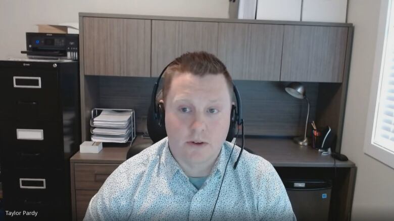 Taylor Pardy, a senior specialist in market analysis, sits in an office and wears a headset for an online interview. He wears a blue shirt.