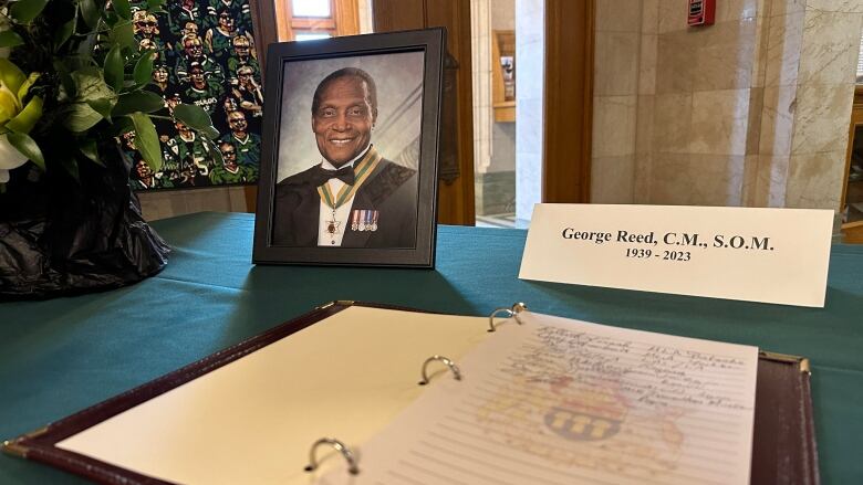 Photo of man in suit sits beside guest book.