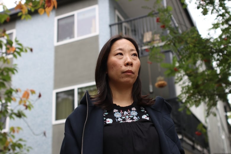 A woman wearing a blue sweater is looking out with a blue building in her background. 