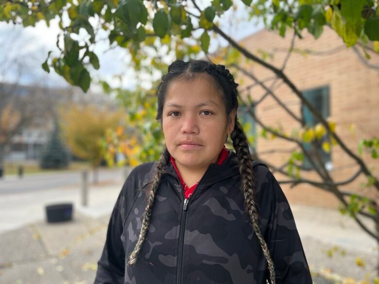 A woman stands near a tree, wearing braids