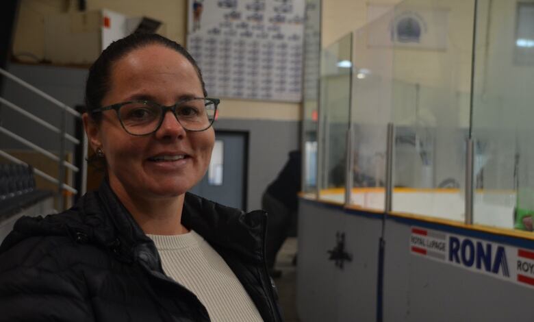 A woman with glasses sits in the stands at a hockey arena 