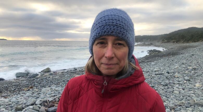 Woman standing in front of the ocean, she is wearing a hat and coat.