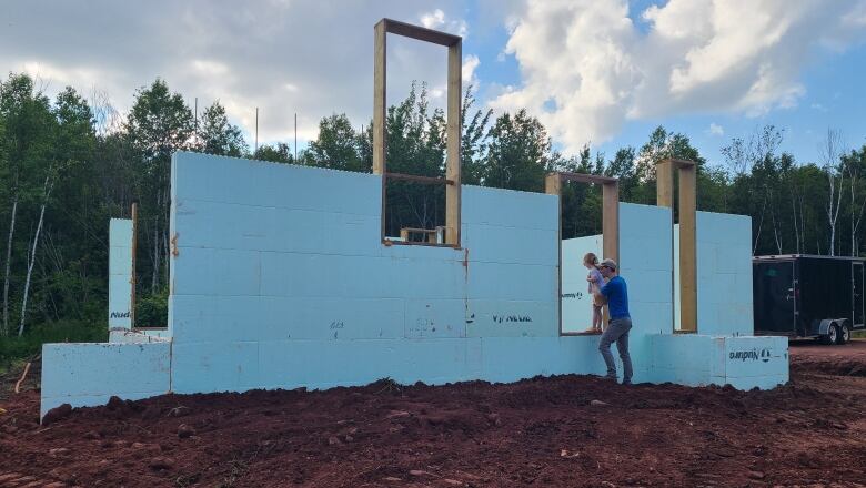 A man stands next to a girl as they both look at a partially-constructed house.