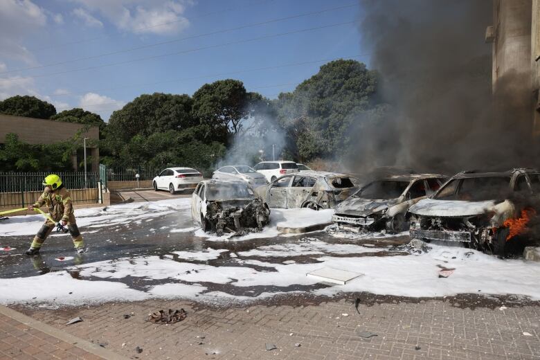 A firefighter works to put out a fire that began following a rocket attack and which engulfed cars parked near a building in Ashkelon, Israel.