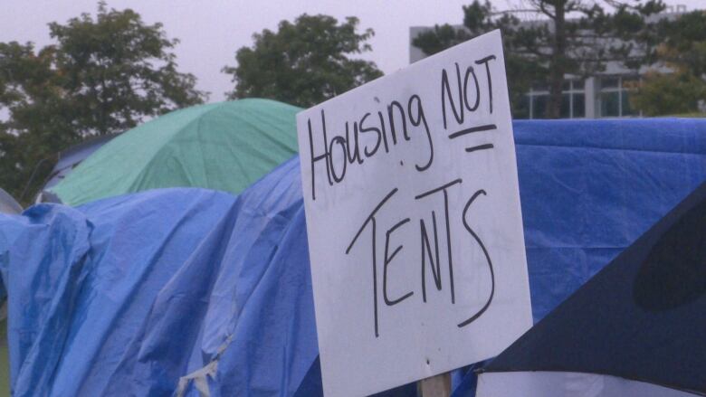 A handwritten sign is pictured in front of tents, which reads 