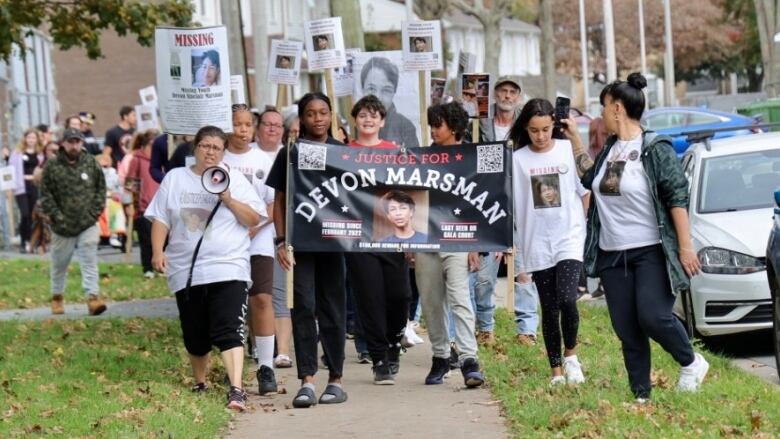 A crowd of people are walking down the side walk holding signs. 