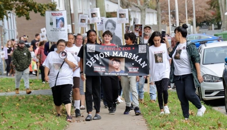 A crowd of people are walking down the side walk holding signs. 