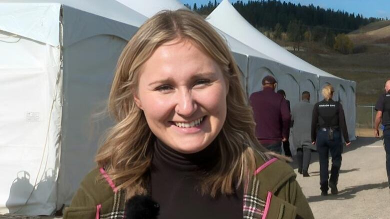 A woman with blonde hair is seen smiling at the camera  with tents in the background.