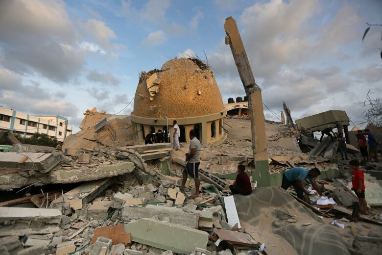 People stand on a large pile of concrete rubble in front of a collapsed dome. 