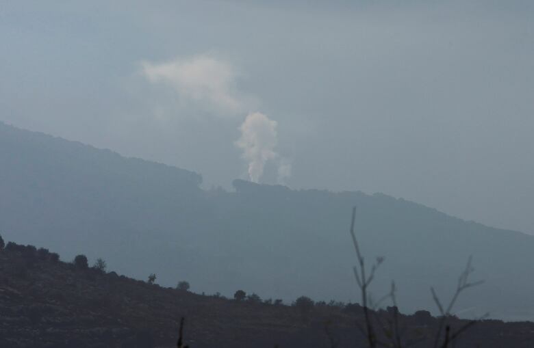 Smoke rises over a mountain in the distance. 